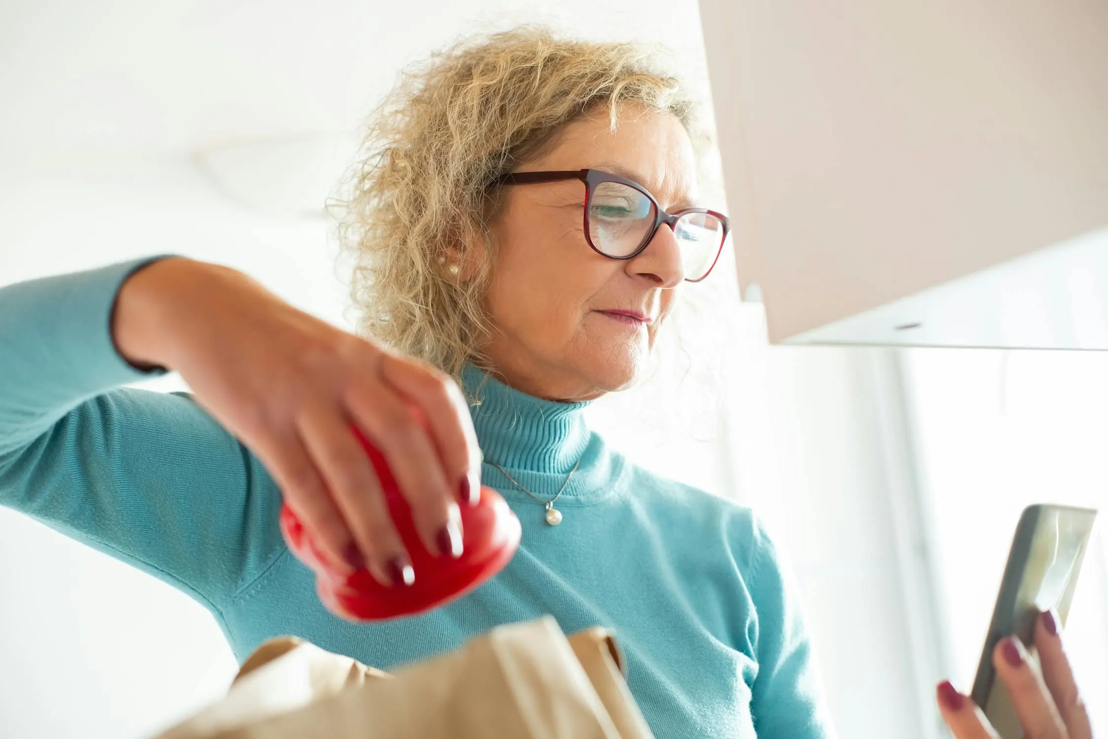 A senior woman at home in her kitchen with her phone within reach